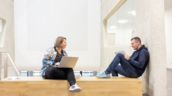 Eine Studentin und ein Student sitzen mit ihren Laptops nebeneinander