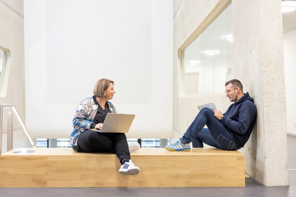 Eine Studentin und ein Student sitzen mit ihren Laptops nebeneinander