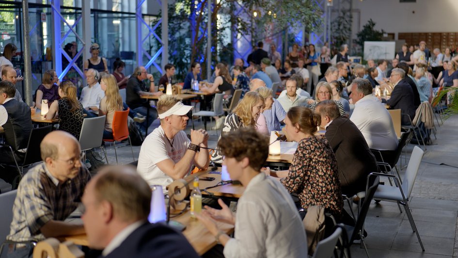 Scientists and visitors sit at tables opposite each other at the Salon of Science and engage in dialogue. 