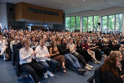 Das Publikum in der Aula steht und klatscht begeistert, der Saal ist bis zum letzten Platz besetzt. (öffnet Vergrößerung des Bildes)