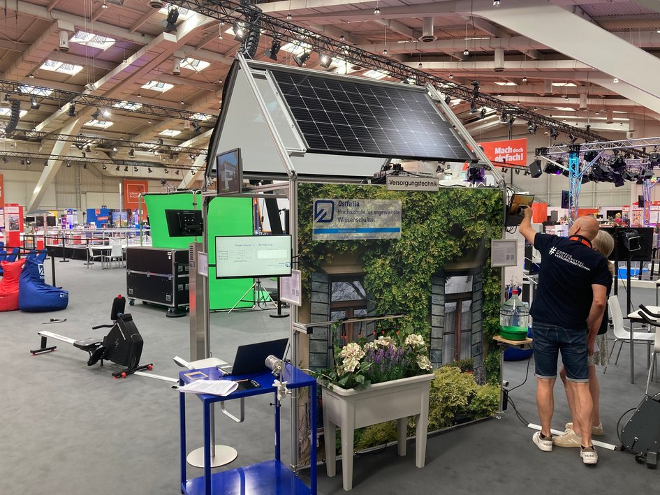 Das Powerhouse der Fakultät Versorgungstechnik auf der IdeenExpo. Rechts neben dem Powerhouse zeigt ein Mitarbeiter der Fakultät einem Besucher einer Besucherin das Powerhouse.