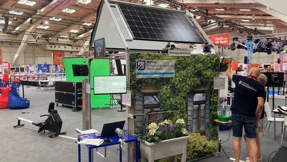 Das Powerhouse der Fakultät Versorgungstechnik auf der IdeenExpo. Rechts neben dem Powerhouse zeigt ein Mitarbeiter der Fakultät einem Besucher einer Besucherin das Powerhouse.