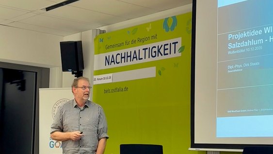Dirk Staats stands at the lectern and gives his presentation at the Sustainability Forum. Behind him you can see part of his PowerPoint slide.