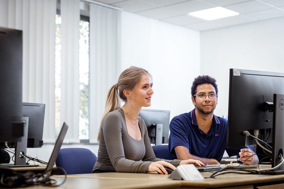 Two students are sitting in front of a screen.