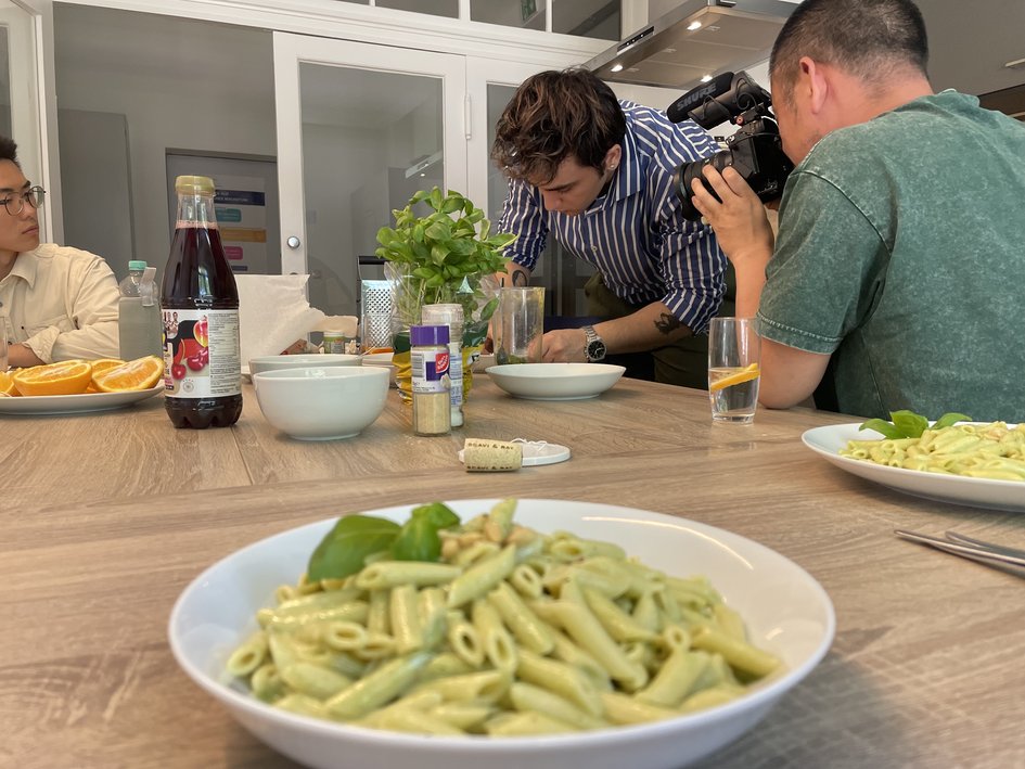 Pasta steht auf dem Tisch. Im Hintergrund sind Studierende.