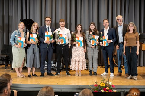 Gruppe von Absolvent*innen des Weiterbildungsmasters Sozialmanagement auf der Bühne, flankiert von Ina Struckmann-Pröve und Prof. Dr. Georg Kortendieck. (öffnet Vergrößerung des Bildes)