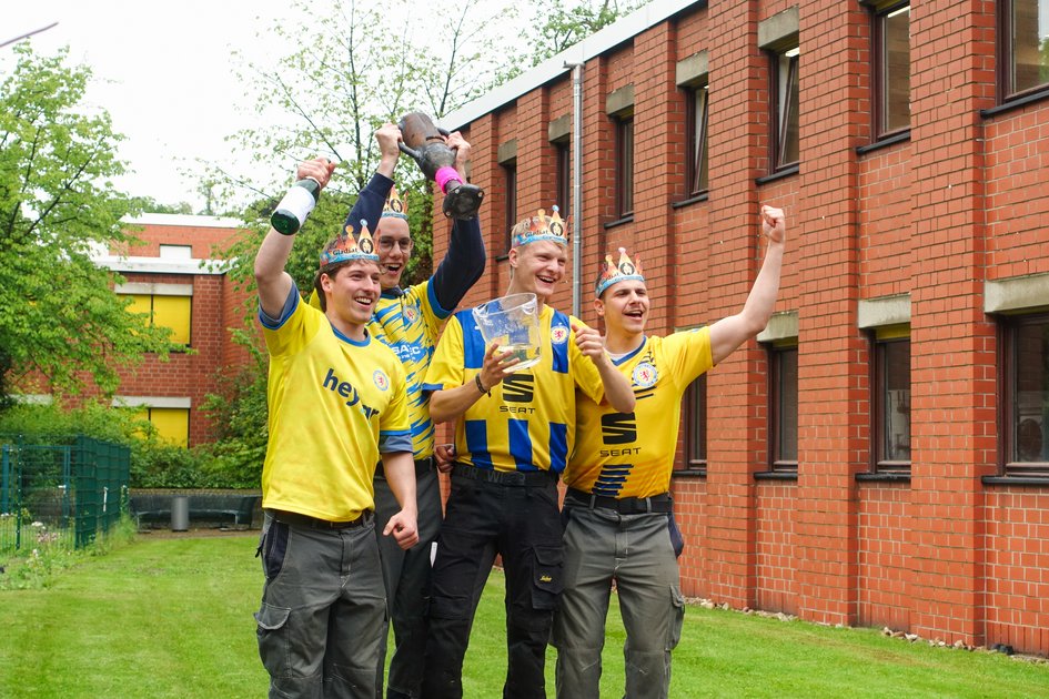Gruppenbild der diesjährigen Gewinner vom Wettbewerb Gladiatrohr 2026. Vier Studierende jubeln und tragen Eintracht Braunschweig Trikots. (öffnet Vergrößerung des Bildes)