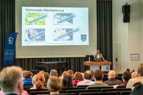 Ein Bild aus der Perspektive eines Zuschauers, wie er in die Menge der Aula Richtung Präsentation schaut. (öffnet Vergrößerung des Bildes)