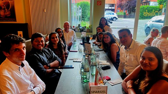 A group of 11 people are sitting around a long table in a restaurant and they are smiling at the camera.