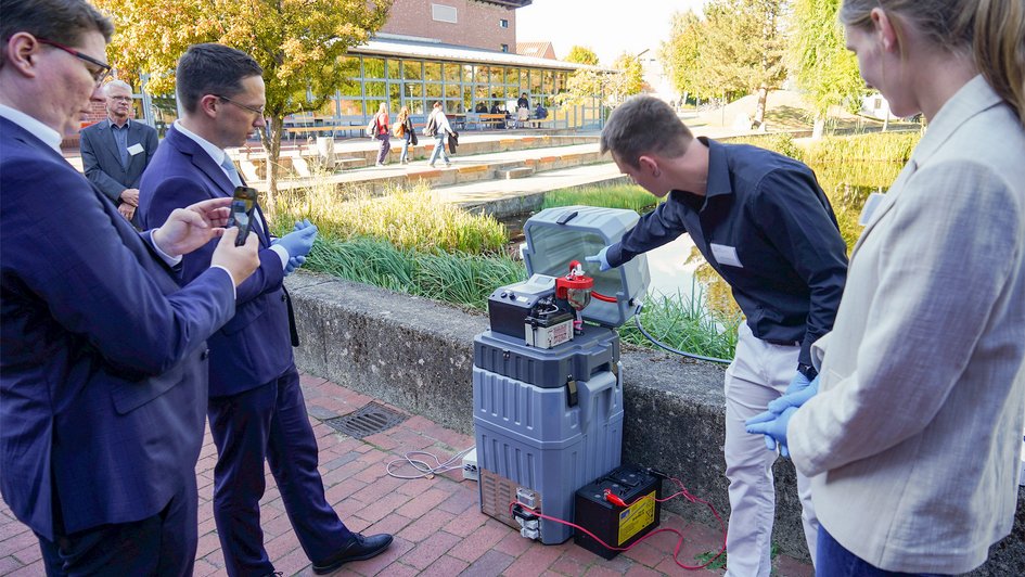 Pressefoto (Nadine Zimmer/Ostfalia): Minister Falko Mohrs an der Station zur Probenentnahme mit den Ostfalia-Forschenden Jakob Waldeck und Marie Meißner. Der Minister konnte hier selbst eine Wasserprobe aus dem Campus-Teich nehmen.