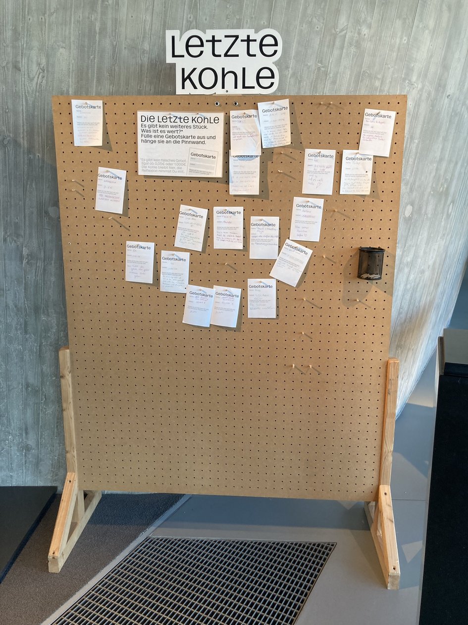 Ausstellungsstation „Letzte Kohle“ mit einer Pinnwand, an der handschriftlich ausgefüllte Gebotskarten befestigt sind.