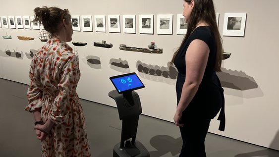 Museumsbot Carl spricht im Museum mit zwei Frauen