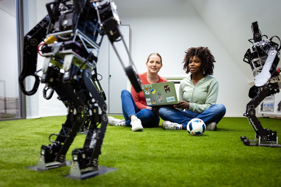 Zwei Studierende der Ostfalia Hochschule steuern an einem Labor der Informatik am Campus Wolfenbüttel einen Roboter, der Fußball spielen kann.