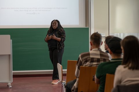 Dr des. Sandrine Bakoben stands in front of the audience and talks about the research project. (opens enlarged image)