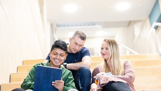 Studierende sitzen auf der Treppe und schauen auf ein Notebook