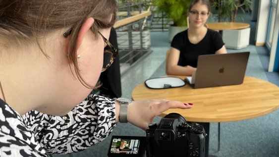 Interview-Setting mit einer Person und Kamera und einer anderen Person am Laptop. Beide bereiten sich auf das bevorstehende Interview vor. 