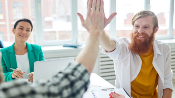 Auf dem Bild ist ein fröhlicher Mann zu sehen, der mit einem anderen Mann die Hand "abklatscht" als Zeichen der Einigkeit und Zusammengehörigkeit