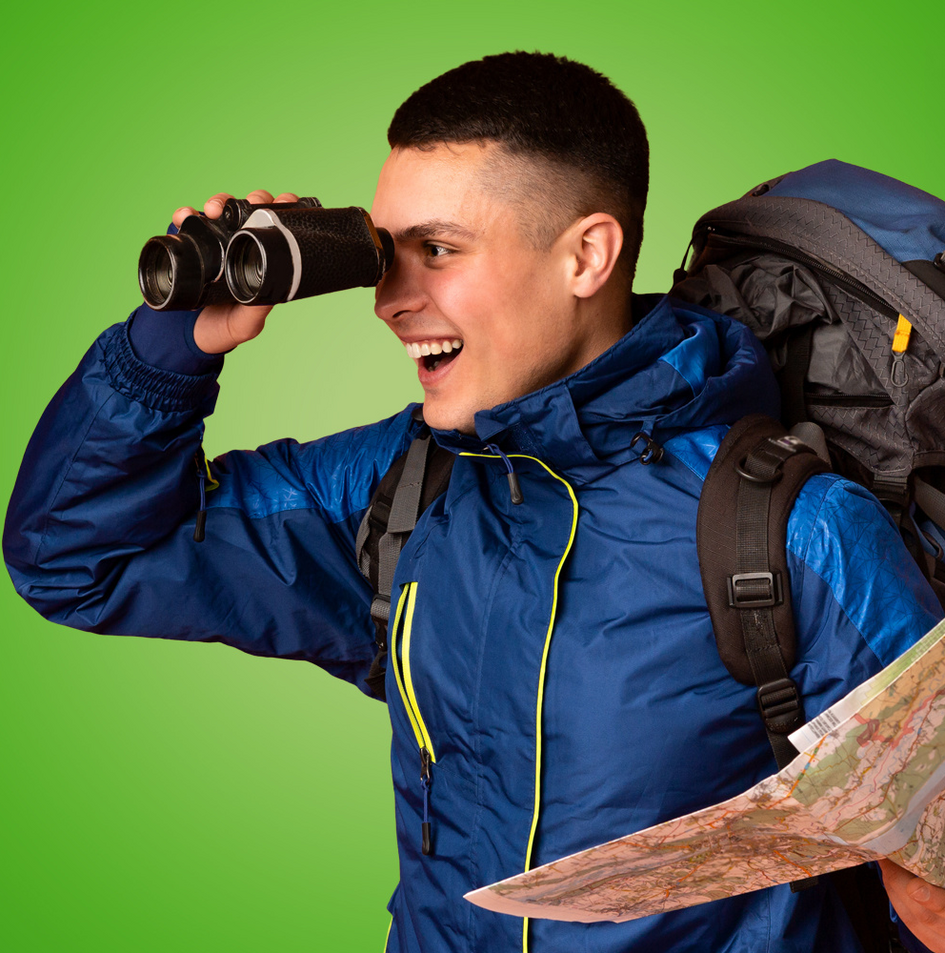 Junger Mann schaut durch Fernglas und hält eine Landkarte (öffnet Vergrößerung des Bildes)