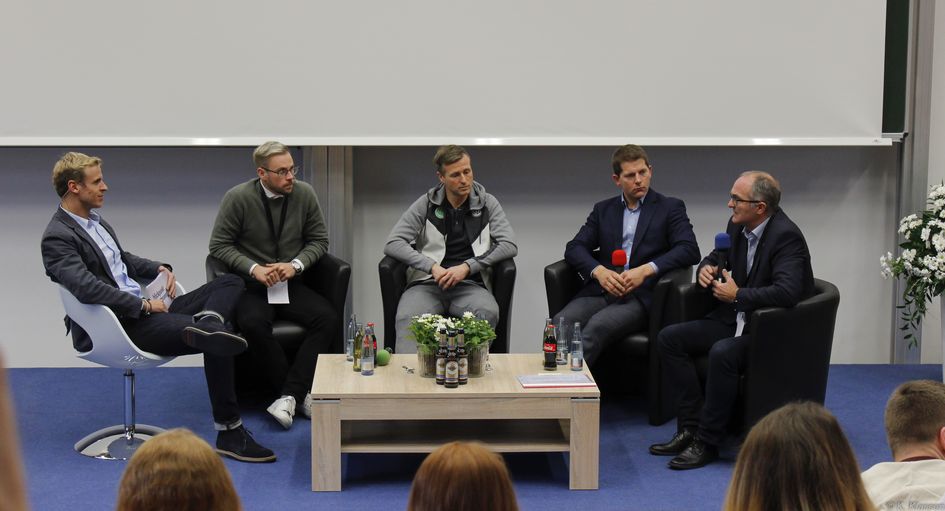Vier Referenten und ein Moderator sitzen auf der Bühne in einer Diskussionsrunde.