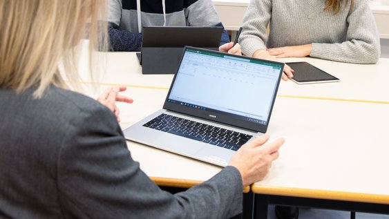 Drei Personen sitzen am Tisch und besprechen sich. Im Vordergrund ist ein Laptop.