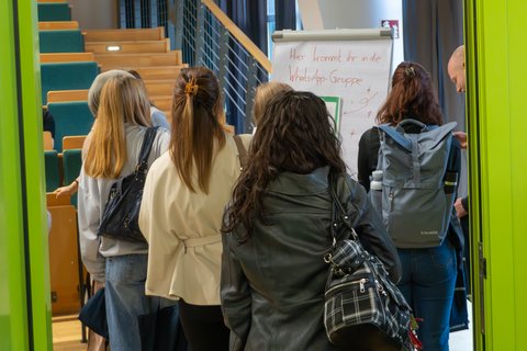 Erstsemester stehen vor einem Flipchart, auf dem in eine WhatsApp-Gruppe eingeladen wird. (öffnet Vergrößerung des Bildes)