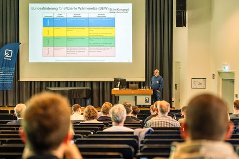 Ein Bild aus der Perspektive eines Zuschauers, wie er in die Menge der Aula Richtung Präsentation schaut. (öffnet Vergrößerung des Bildes)