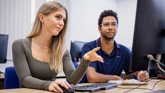 Studierende der Ostfalia Hochschule schauen auf einen Bildschirm und unterstützen sich gegenseitig.