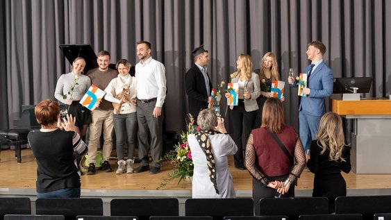 Absolvent:innen lassen sich auf der Bühne der Aule mit ihren Urkunden fotografieren.