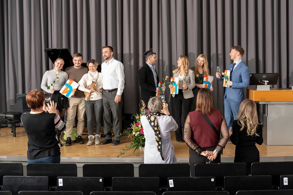 Absolvent:innen lassen sich auf der Bühne der Aule mit ihren Urkunden fotografieren.