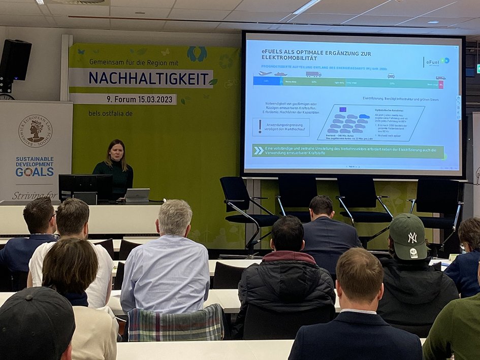 Marlene Hermfisse von der eFuel Alliance steht am Rednerpult und hält ihren Vortrag, auch ein Teil des Auditoriums ist zu sehen, auf einer Leinwand auch die Präsentation der Vortragenden.