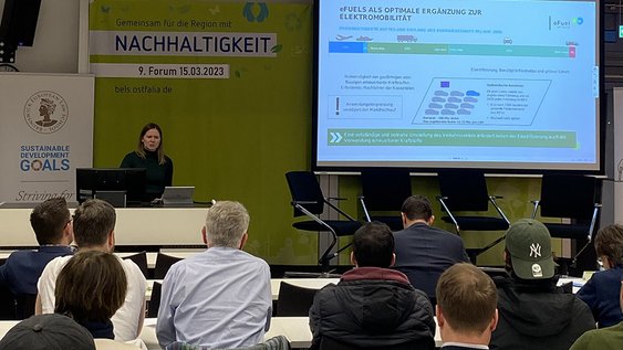 Marlene Hermfisse von der eFuel Alliance steht am Rednerpult und hält ihren Vortrag, auch ein Teil des Auditoriums ist zu sehen, auf einer Leinwand auch die Präsentation der Vortragenden.