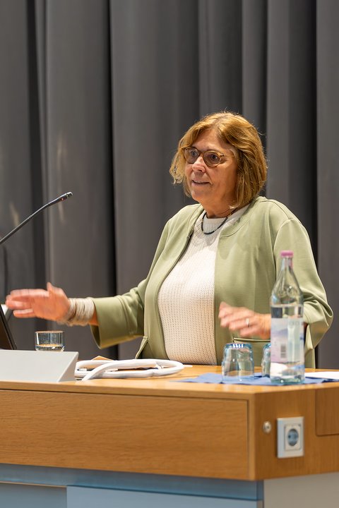 Dekanin Prof. Dr. Sandra Verena Müller spricht an einem Rednerpult mit Mikrofon in der Aula. (öffnet Vergrößerung des Bildes)