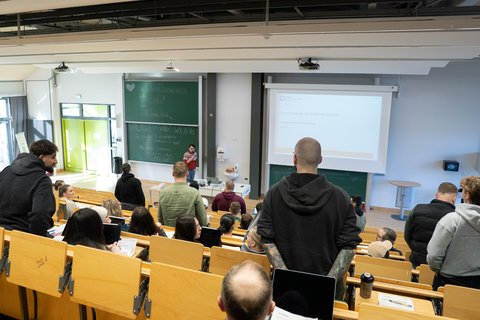 Einzelne Studierende im Hörsaal sind stehen von hinten zu sehen, während Helge Keller vorne seht und ihnen Fragen stellt. (öffnet Vergrößerung des Bildes)