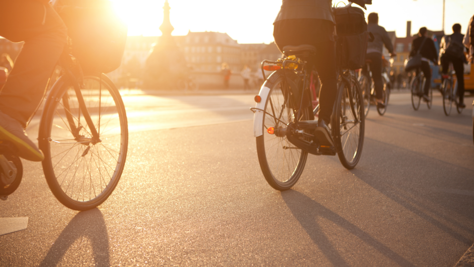 Mehrere Fahrradfahrer:innen die in einer Stadt bei Sonnenuntergang fahren.