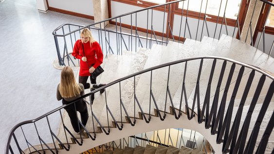 Zwei Personen unterhalten sich auf den Stufen einer langen, geschwungenen Treppe.