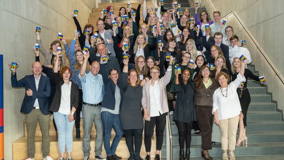 Absolventen und Absolventinnen halten jubelnd ihre Ostfalia-Tassen hoch