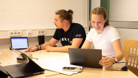 Zwei Studierende am Laptop, die zusammen arbeiten.