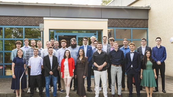 26 Absoventinnen und Absolventen der Fakultät Bau-Wasser-Boden posieren für ein Gruppenbild vor dem Haupteingang.