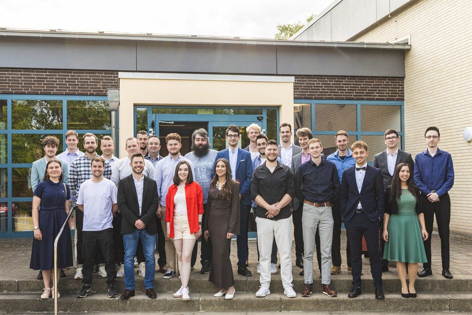 26 Absoventinnen und Absolventen der Fakultät Bau-Wasser-Boden posieren für ein Gruppenbild vor dem Haupteingang.