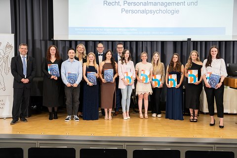 Gruppenbild eines Teils der anwesenden Absolventinnen und Absolventen des Bachelor-Studiengangs Recht, Personalmanagement und Personalpsychologie auf der Bühne. (öffnet Vergrößerung des Bildes)