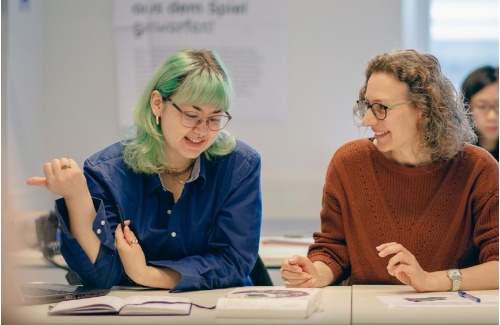Eine Studentin und eine Professorin sitzen zusammen am Tisch und unterhalten sich
