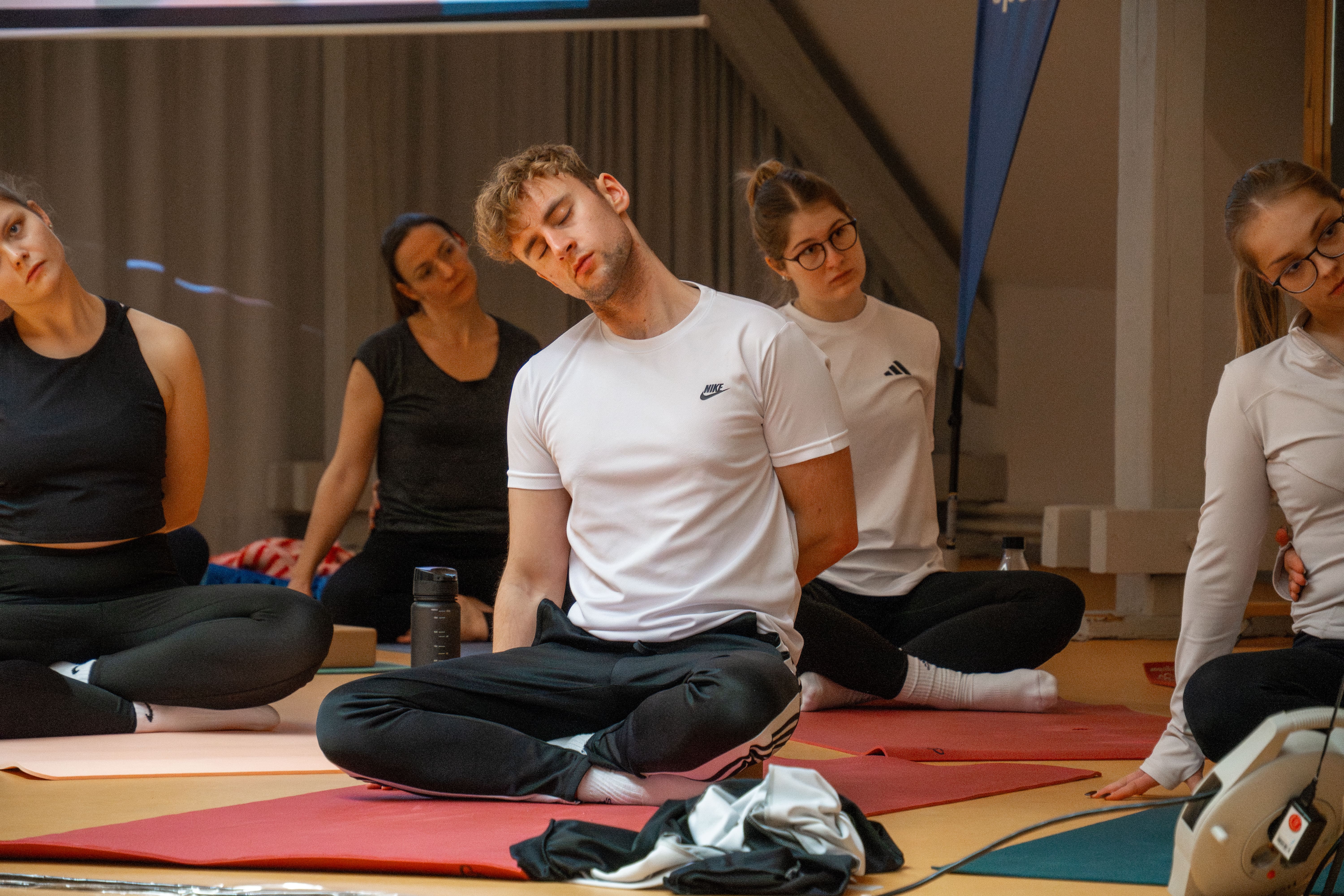 Erfahrene Yoga-Lehrerin führt eine Gruppe von Studierenden durch eine sanfte Dehnübung im Gymnastikraum.