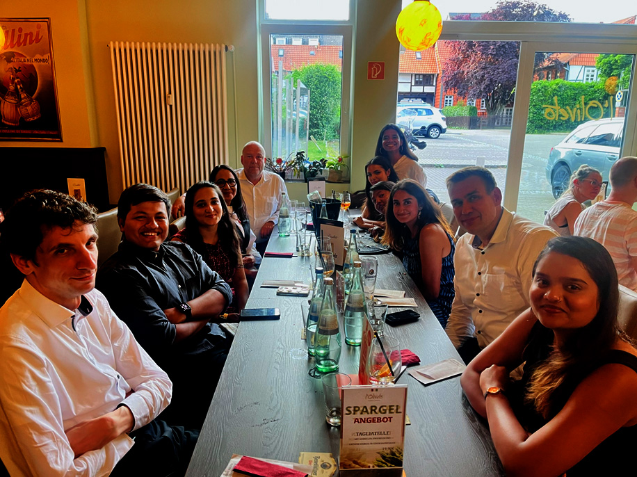 A group of 11 people are sitting around a long table in a restaurant and they are smiling at the camera.